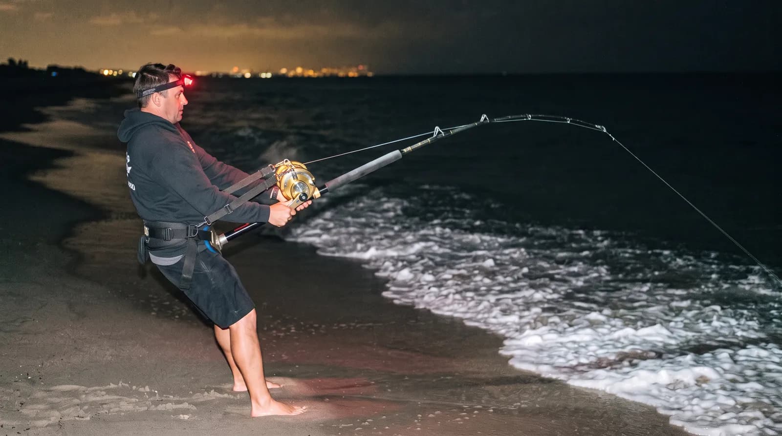 Angler clipped into a fighting harness on a dark beach
